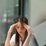 HABITOS  NAO USAR APOS ESSA DATA 05-08-2024 EM CASO DE DUVIDA CONSULTE A FOTOGRAFIA Photo of a tired woman keeps a hand on her head at the wooden working desk after finishing work hard. photo saltdium/adobe.stock